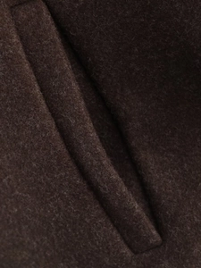 Macro shot of dark brown wool coat showing premium fabric texture and fine pocket stitching