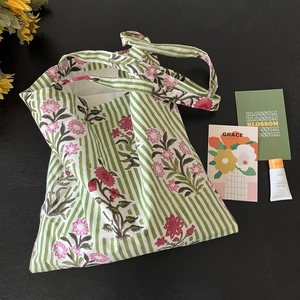 Flat lay of green striped cotton tote bag with pink floral patterns and blossom card