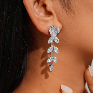 Macro shot of silver drop earrings with heart and leaf-shaped zircon stones on a model