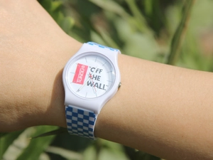 Detail shot of a white casual watch with a blue checkered strap on a wrist outdoors