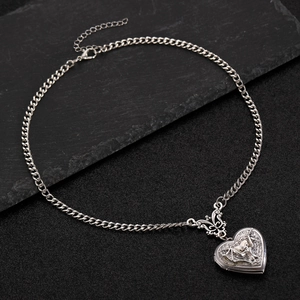 Detail of silver heart locket necklace with vintage angel relief on dark stone background