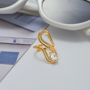 Detail of gold hollow wave ring with a teardrop-shaped zircon on a modern white desk