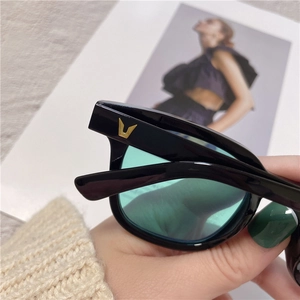 Close-up of black acetate sunglasses frame with green lenses and gold V detail