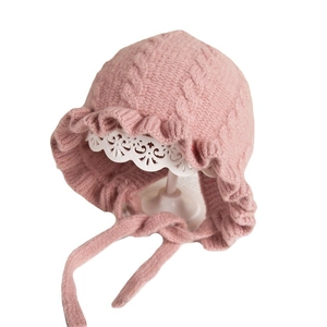 Pink knit baby hat with ear flaps, lace ruffles, and decorative cable stitch patterns