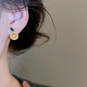 Detailed macro view of orange slice zircon stud earring with green leaf and golden base