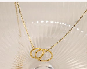 Detail of gold double-ring pendant necklace displayed on textured glass with soft lighting