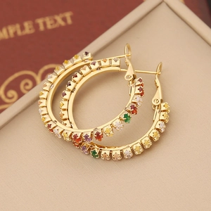 Detail of gold hoop earrings with claw-set colorful zircons on a beige jewelry tray