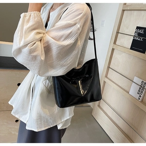 Sac seau chic en cuir verni porté par un mannequin dans un décor de pièce épuré