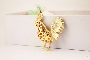 Detailed close-up of golden rooster pendant featuring heart-shaped cutout and metal texture