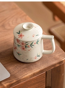 Detailed view of hand-painted peach blossoms on ceramic mug with lid on wooden table
