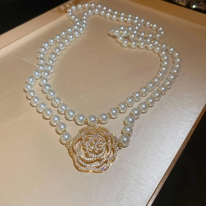 Détail du pendentif fleur de camélia doré sur un collier de perles double élégant