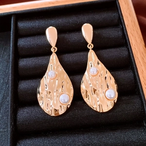 Détail de boucles d'oreilles gouttes dorées 18K avec métal texturé et perles