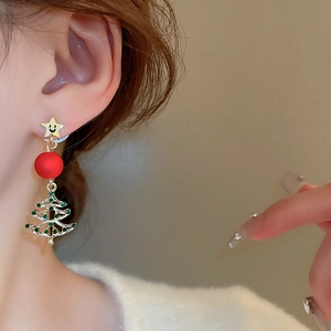 Close-up of model wearing Christmas tree earrings with green rhinestones and star stud