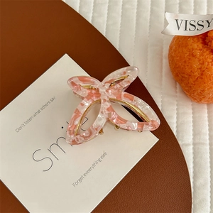Detail of pink floral butterfly hair claw clip with golden metal fastener on textured background