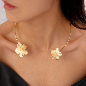 Detail eines minimalistischen Goldblumen-Halsreifs mit gebürsteter Metallstruktur am Modell
