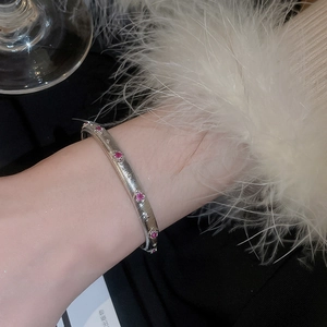 Makroaufnahme eines silbernen gebürsteten Armbands mit eingelegten rosa Edelsteinen