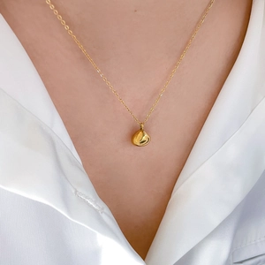 Detailed view of a golden teardrop pendant necklace worn on a white textured shirt