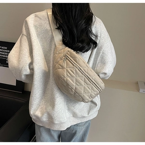 Close-up of beige quilted crossbody bag worn by a model in a minimalist indoor setting