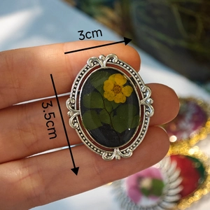 Macro view of handmade resin brooch with yellow dried flowers and silver scrollwork