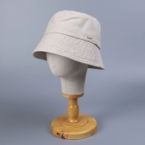 Detail view of a beige bucket hat with a premium JNXY metal logo on a model stand