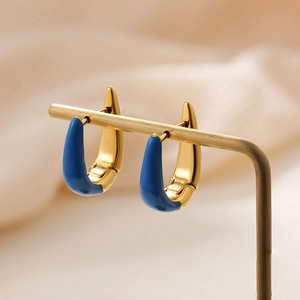 Macro shot of U-shaped gold earrings with blue enamel finish on a metal jewelry stand