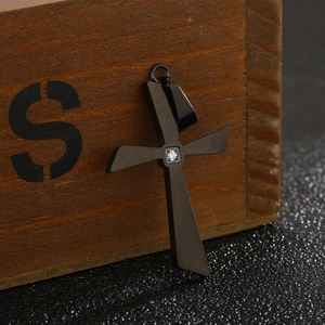 Close-up of polished black stainless steel cross pendant with a single sparkling diamond inlay