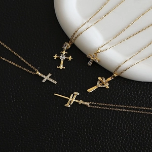 Five styles of gold cross necklaces with cubic zirconia on black leather and white tray