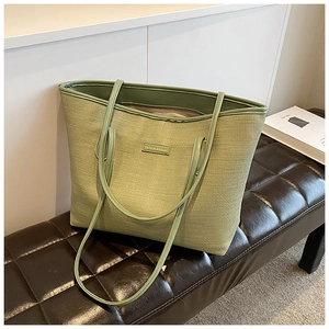 Detail of green woven tote bag with gold metal plate on a leather bench setup