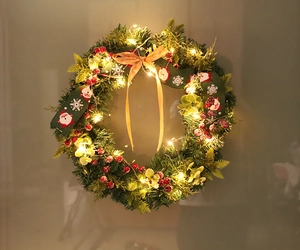 Detail of Christmas wreath with green pine needles, red berries, and warm LED light string