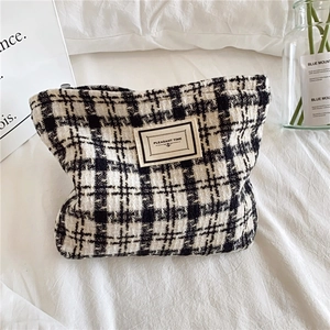 Large plaid tweed makeup bag with checkerboard pattern and zipper on white bedding