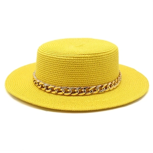 Detail view of woven straw boater hat featuring a chunky gold metal chain decoration
