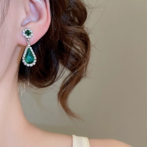Close-up of elegant pear-cut emerald earrings with shimmering zircon halo on a model