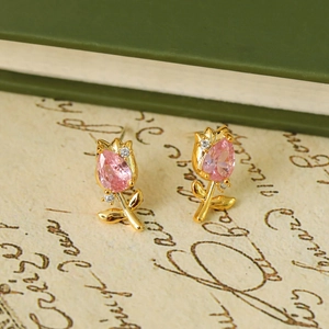 Gold tulip earrings with pink zircon stone set on a vintage paper and green book background