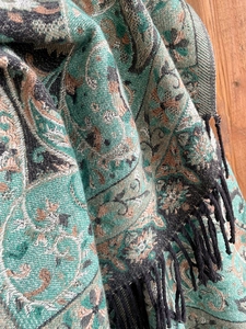 Detail of teal paisley pattern woven scarf with elegant black tassels on wood surface