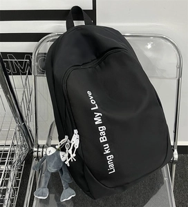 Detail of black nylon backpack featuring white text print and a grey frog plush pendant