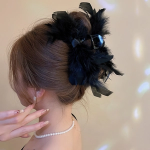 Detail of elegant black feather hair claw clip with satin bow on woman's updo hairstyle