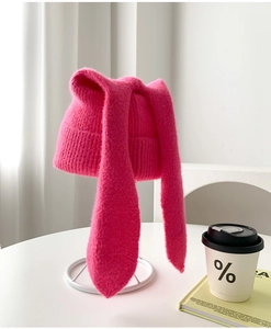 Pink knit hat with long bunny ears shown on a table with a coffee cup and book