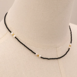 Détail du collier de perles noires avec cœurs blancs et accents dorés sur mannequin