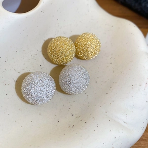 Macro shot of gold and silver textured hemispherical stud earrings on a ceramic tray