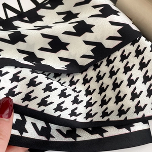 Macro shot of houndstooth silk scarf with pink accents and elegant black edge detail