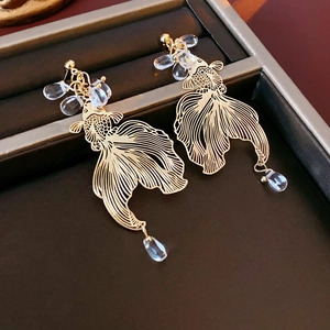 Detail of golden hollow koi fish earrings with elegant transparent water drop beads