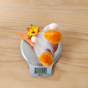 Macro view of a 33g autumn gnome plush with sunflower on a digital kitchen scale