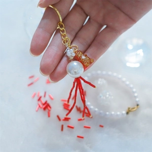 Golden glitter bear keychain with white faux pearl and red coral bead tassels held by hand