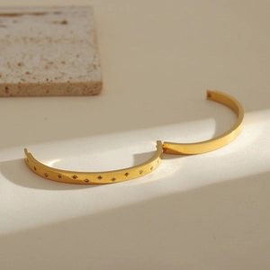 Golden titanium steel bangle with star patterns and pavé rhinestones on beige stone