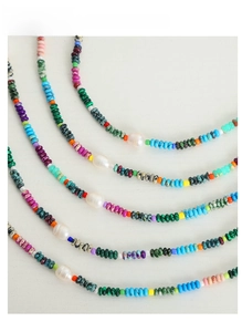 Flat lay of colorful ethnic beaded necklaces with white pearls on a light wood surface