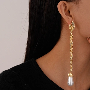 Close-up of long gold leaf tassel earrings with a water drop pearl on a female model