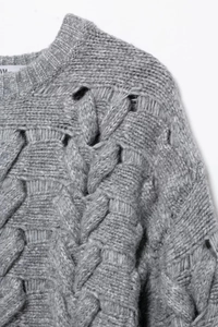 Detail of grey cable-knit sweater showing intricate shoulder weave and hollow-out texture