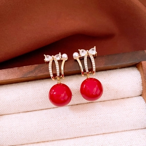 Detail of 18K gold plated bow earrings with sparkling zircons and large red round beads