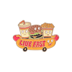Fast food enamel pin featuring cartoon burger and fries on a Live Fast hot dog skateboard