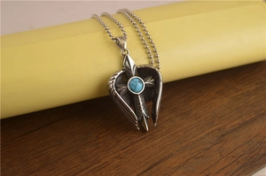 Gros plan du pendentif ailes argentées avec incrustation de turquoise et détails croix